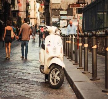 vespa on the street and the couple walking behind it holding hands