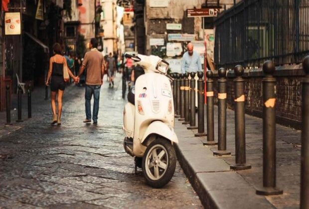 vespa on the street and the couple walking behind it holding hands